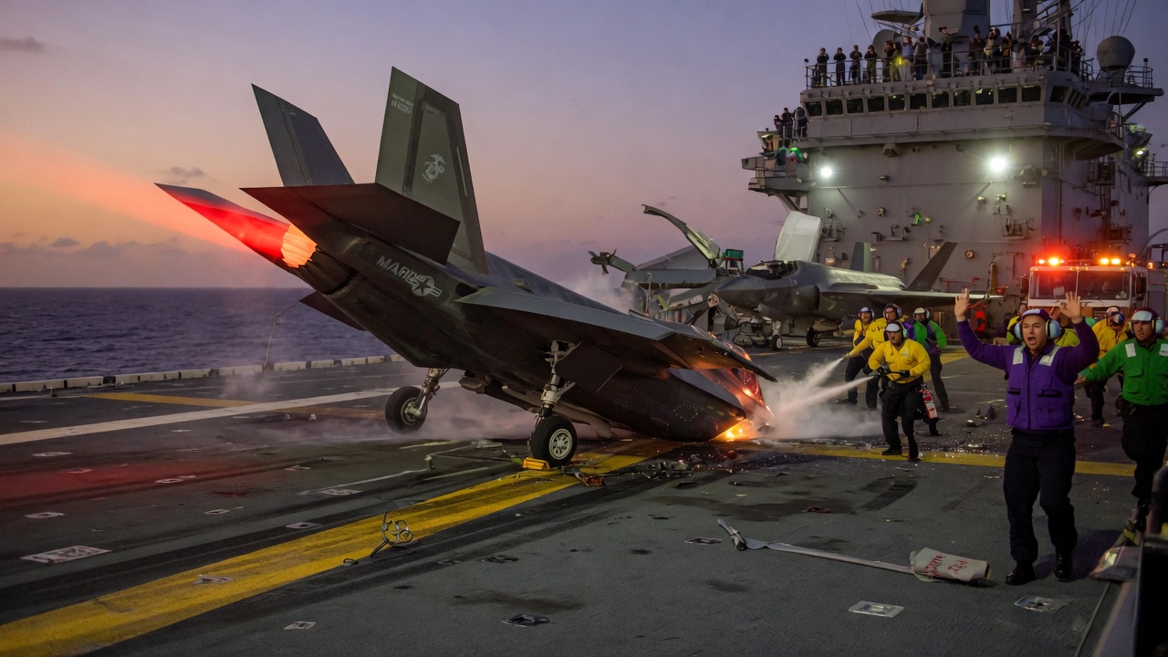 Cartoon F-35 jet on fire in a field with a five-star badge on the ejection seat and a frowning 'needs improvement' sticker on the fuselage.